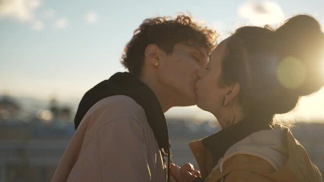 4k Lgbt couple in love kisses on background of city spbd. Close view of two young lesbian women kissing and hugging with tenderness, standing on rooftop outdoors. Happy gay people show affection
