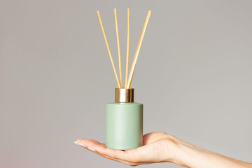 a female hand holding a green bottle with an aromatic diffuser and bamboo or rattan sticks isolated...