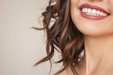a close-up photo of a part of the face of a beautiful young laughing woman with curly dark hair, bright lipstick on her lips and a beautiful smile isolated on a beige background
