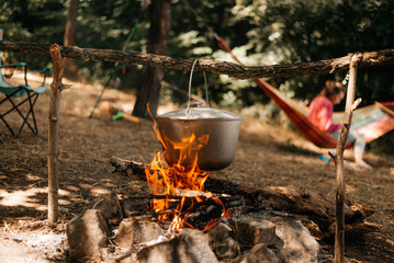 Travel a kettle over a fire burning on the river and sunset backgroun. Cooking over a campfire