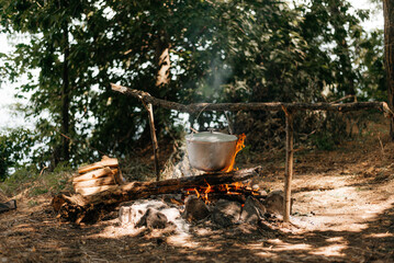 Travel a kettle over a fire burning on the river and sunset backgroun. Cooking over a campfire