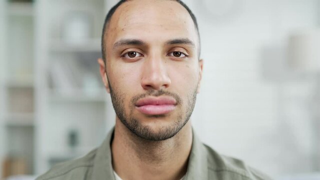 Portrait serious confident young adult man looking at camera indoors. Headshot closeup handsome male of mixed race at home pensive expression Latino multiracial ethnicity businessmansad offended face