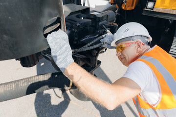 Mechanic repairing hydraulic hose in drilling machine, exploration drilling. Man in hard hat industrial worker