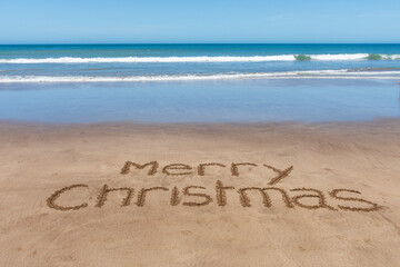 Merry Christmas text written on the sand of the beach.