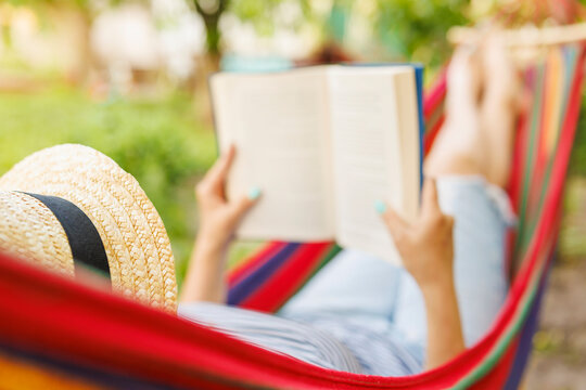 Young woman reading book while lying in comfortable hammock at green garden