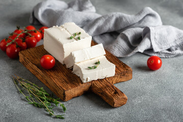 Fresh feta cheese with thyme and cherry tomatoes, gray concrete background. Side view, selective focus.