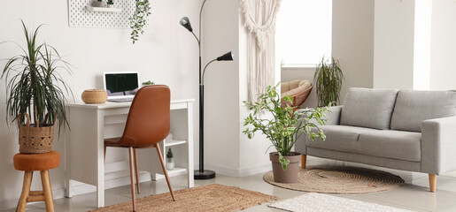 Interior of light living room with grey sofa, modern workplace and houseplants