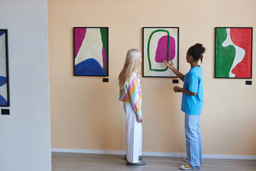 Minimal full length portrait of two teenagers girls discussing modern art in gallery or museum, copy space