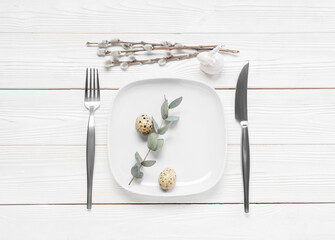 Beautiful Easter table setting with quail eggs, eucalyptus and willow branches on white wooden background