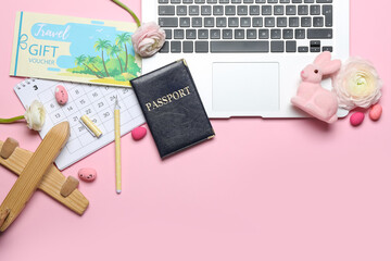 Laptop with travel accessories, flowers, Easter eggs and rabbit on pink background