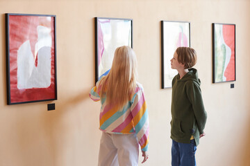 Minimal back view of wo teenagers looking at modern art in gallery or museum