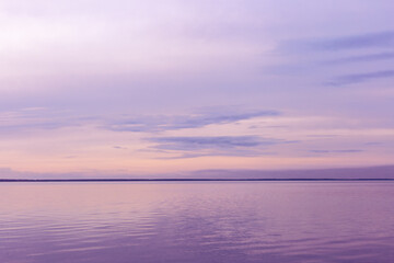 Minimal Colorful sky background on sunset, purple pastel color clouds and surface water on lake Ik. Nature abstract composition with reflections on water, natural blue pink shades of skyline