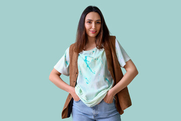 Stylish young woman in tie-dye t-shirt and waistcoat on light blue background