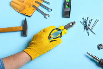 Male hand in gloves holding pliers near different instruments on blue background