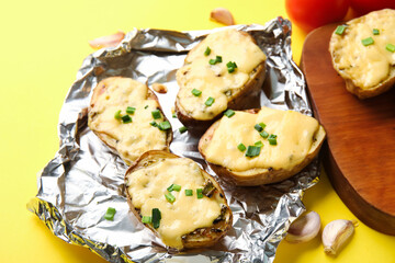 Aluminium foil with tasty baked potato on yellow background, closeup