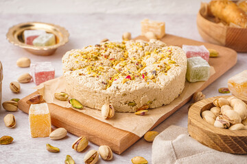 Wooden board of tasty Tahini halva with pistachios on light background