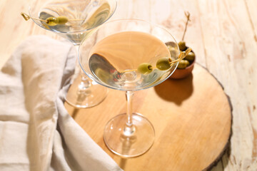 Glasses of tasty martini and olives on light wooden table