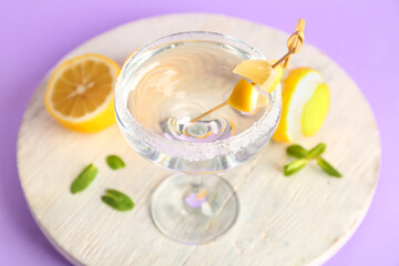 Glass of tasty martini and lemon on purple background