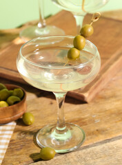 Glass of tasty martini and olives on wooden table
