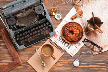 Cup of coffee with notebook, typewriter, newspaper, bun and map on wooden background