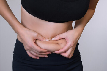 close up photo of young woman hand holding excessive belly fat on gray background. Health concept