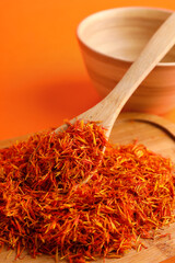 Wooden board and spoon with pile of saffron on orange background