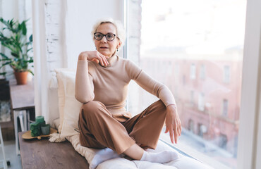 Ponder senior woman sitting on windowsill