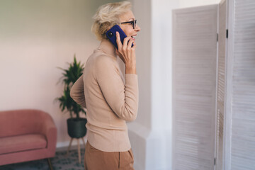 Cheerful mature woman with smartphone standing in living room