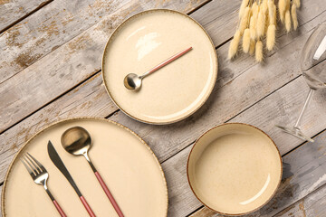 Table setting with clean plates, cutlery and dried lagurus on wooden table