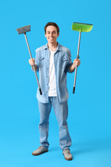 Young man with broom and dustpan on blue background
