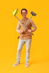 Young man with broom and dustpan on yellow background