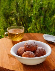 Round cottage cheese donuts, sprinkled with powdered sugar, in a white bowl on a round wooden background. Donut recipes.