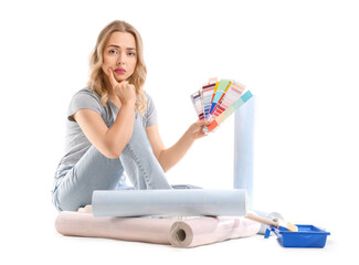 Upset young woman with color palettes and wallpaper rolls sitting on white background