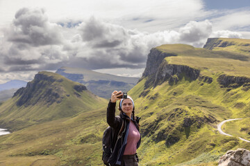 Young woman making selfie with smartphone on mountain range Quiraing. It is a geological formation...