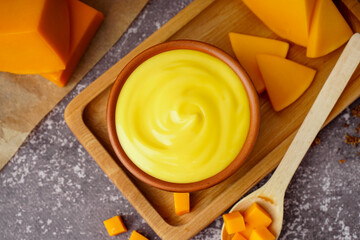 Board with bowl of tasty cheddar sauce and cheese chunks on black grunge background