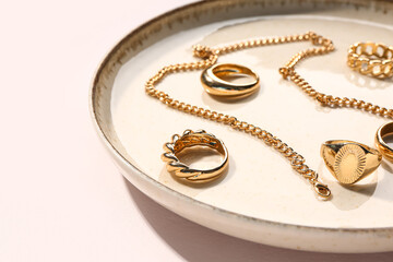 Plate with golden rings and necklace on white background