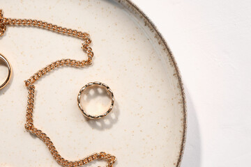 Plate with golden rings and necklace on white background