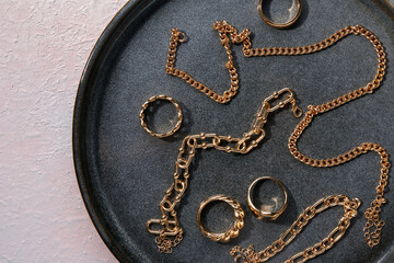 Plate with beautiful golden jewellery on pink textured background