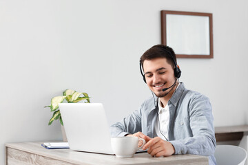 Male technical support agent with laptop and coffee in office