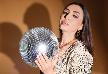 Naklejka premium Fashionable beautiful woman in sparkling dress with disco ball on orange background