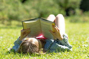 A girl is lying and reading her favorite book on a green meadow covered with yellow flowers in a...