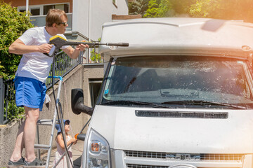 A man washes his motorhome with a brush .Hand washing a car at home on the street.