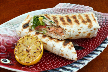 cut grilled salmon fish roll with lemon, garlic sauce, tomato, salad and avocado closeup photo
