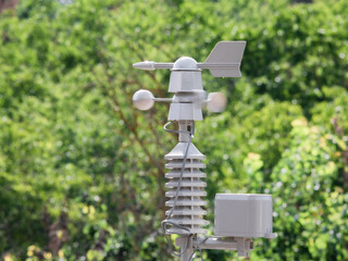 Weather vane marking the direction of the wind and anemometer (wind speed meter) blurred by the action of the air located on top of a weather station - obrazy, fototapety, plakaty