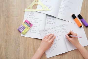 Woman writing math formulas in copybook on wooden table - obrazy, fototapety, plakaty