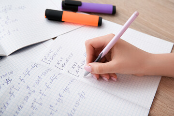 Woman writing math formulas in copybook on wooden table