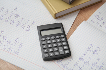 Open copybook with math formulas and calculator on wooden table