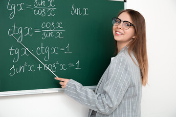 Young math teacher with pointer near blackboard in classroom