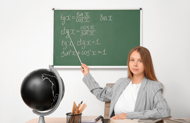 Young math teacher with pointer sitting at wooden table in classroom