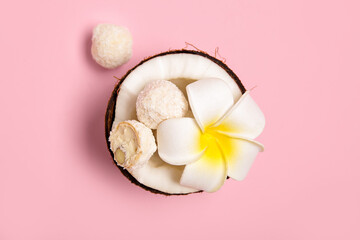 Fototapeta na wymiar Coconut with white chocolate candies and plumeria flower on pink background